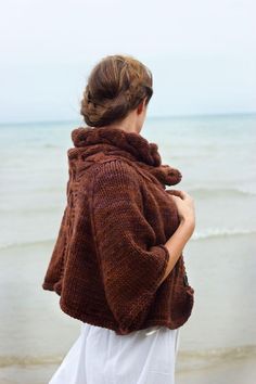 a woman standing on the beach with her back to the camera