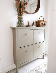 a white dresser with flowers in a vase and a mirror on the wall above it