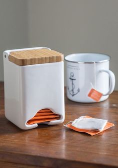 two coffee mugs sitting next to each other on top of a wooden table with orange napkins in front of them