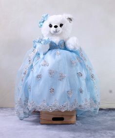 a white teddy bear dressed in a blue dress sitting on top of a wooden box