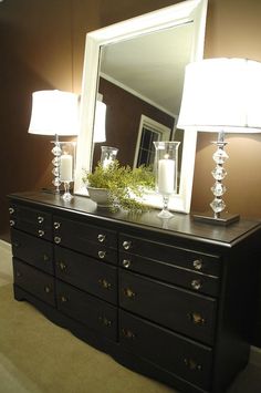 a black dresser with two lamps and a mirror on it's top shelf in front of a brown wall