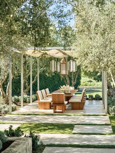 an outdoor dining area in the middle of a garden with lots of trees and grass