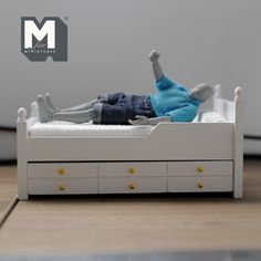 a doll laying on top of a white bed next to a wooden floor and wall