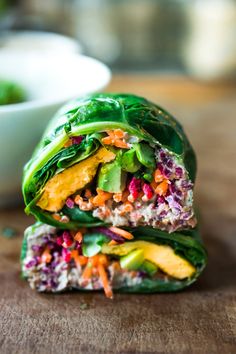 two wraps filled with vegetables sitting on top of a wooden table next to a bowl