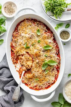 a casserole dish with meat, cheese and herbs in it on a white table