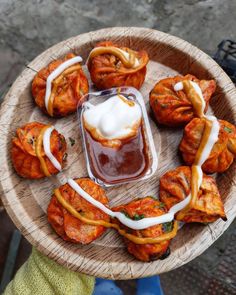 a person holding a wooden plate with food on it and sauce in the middle,