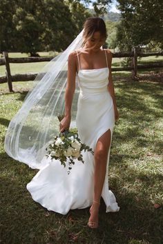 a woman in a white wedding dress holding a flower bouquet and wearing a long veil