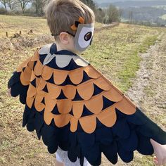 a young boy wearing a bird costume on top of a grass covered field with trees in the background