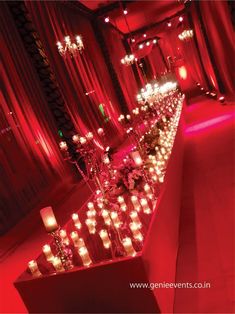 a long table with candles and flowers on it in front of a red curtained wall