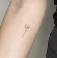 a small single flower tattoo on the left inner arm, with an arrow in the middle