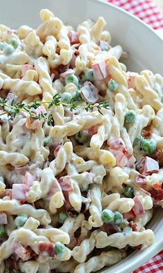 a pasta salad with peas and ham in a white bowl