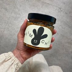 a hand holding a jar of kimchi with a black bunny face on the lid