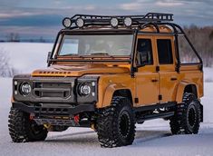 an orange four - door truck is parked in the snow with its lights on and it's hood up