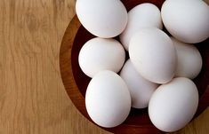 a wooden bowl filled with white eggs on top of a table