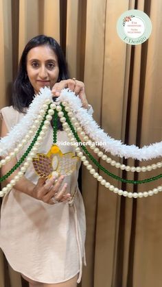 a woman is holding up some white and green beads in front of a curtained window