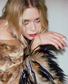 a woman with long hair and blue eyes wearing a feathered dress posing for a photo