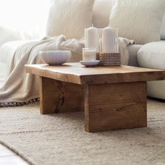 a wooden table with candles on it in front of a white couch and throw pillows