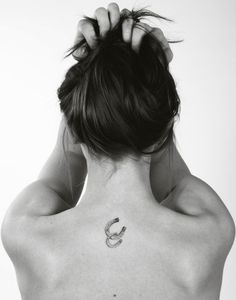 the back of a woman's neck with a horseshoe tattoo on her left side