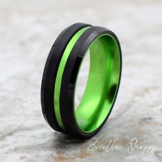 a black and green ring with an inlay on the inside is sitting on a stone surface