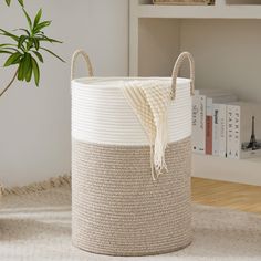 a white and beige basket sitting on top of a rug next to a potted plant