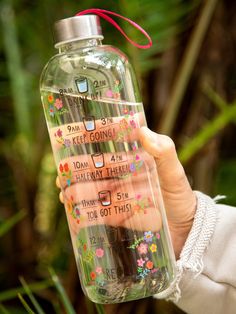 a person holding up a water bottle with writing on it and flowers in the bottom