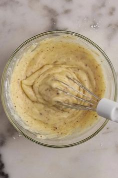 a glass bowl filled with batter sitting on top of a marble counter next to a whisk