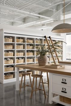 a kitchen with white cabinets and shelves filled with baskets on top of the counter, next to two stools