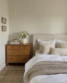 a bed with white linens and pillows in a bedroom next to a wooden dresser