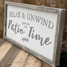 a sign that says relax and unwind youre on patio time next to some flowers