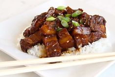 a white plate topped with meat and rice next to chopsticks