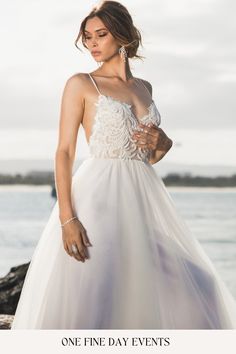 a woman in a white dress standing on rocks near the water with her hand on her hip