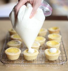 someone pouring icing onto some cupcakes on a cooling rack