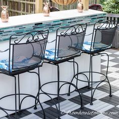 four bar stools sitting on top of a checkered tile floor next to an outdoor kitchen