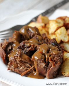 a white plate topped with meat and gravy covered in gravy next to potatoes