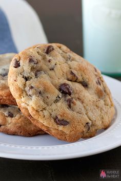 two chocolate chip cookies on a white plate next to a blue napkin and glass of milk