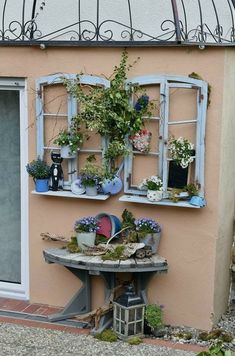 an outdoor table with potted plants on it next to a pink wall and window