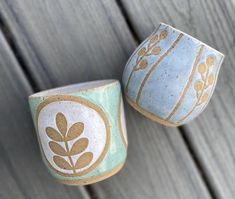 two blue and white cups sitting on top of a wooden table next to each other