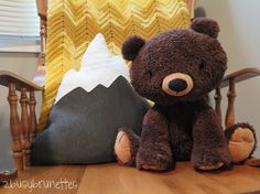 a brown teddy bear sitting on top of a wooden table next to a pillow and chair