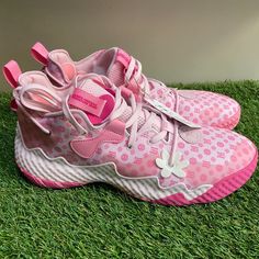 a pair of pink and white shoes sitting on top of green grass in front of a wall