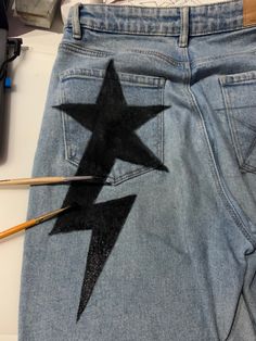 a pair of blue jeans with black stars painted on them and two pencils next to it