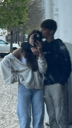 a man and woman standing next to each other taking a selfie in front of a building