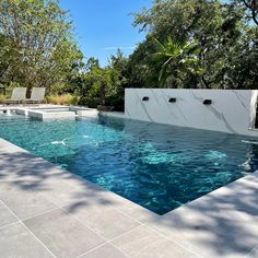 an outdoor swimming pool surrounded by trees and chairs with blue water running through the center