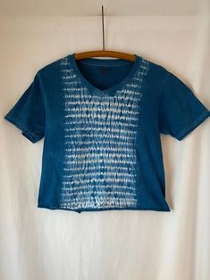 a blue t - shirt hanging on a wooden hanger in front of a white wall