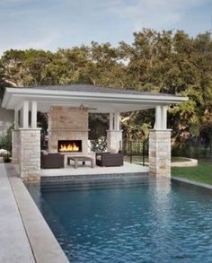 an outdoor living area next to a swimming pool and covered patio with fireplace in the middle