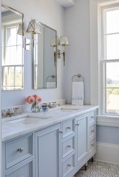 a white bathroom with two sinks and mirrors on the wall next to a large window