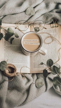 an open book with a cup of coffee on top of it next to some leaves