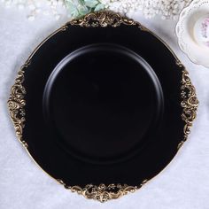 a black and gold plate sitting on top of a table next to some white flowers