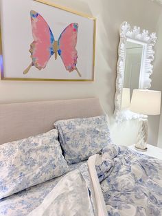 a bed with blue and white comforter next to a framed butterfly painting on the wall