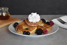 a white plate topped with pancakes covered in whipped cream and berries next to a jar of syrup