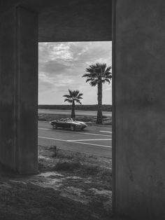 a black and white photo of a car passing under an overpass with palm trees in the background